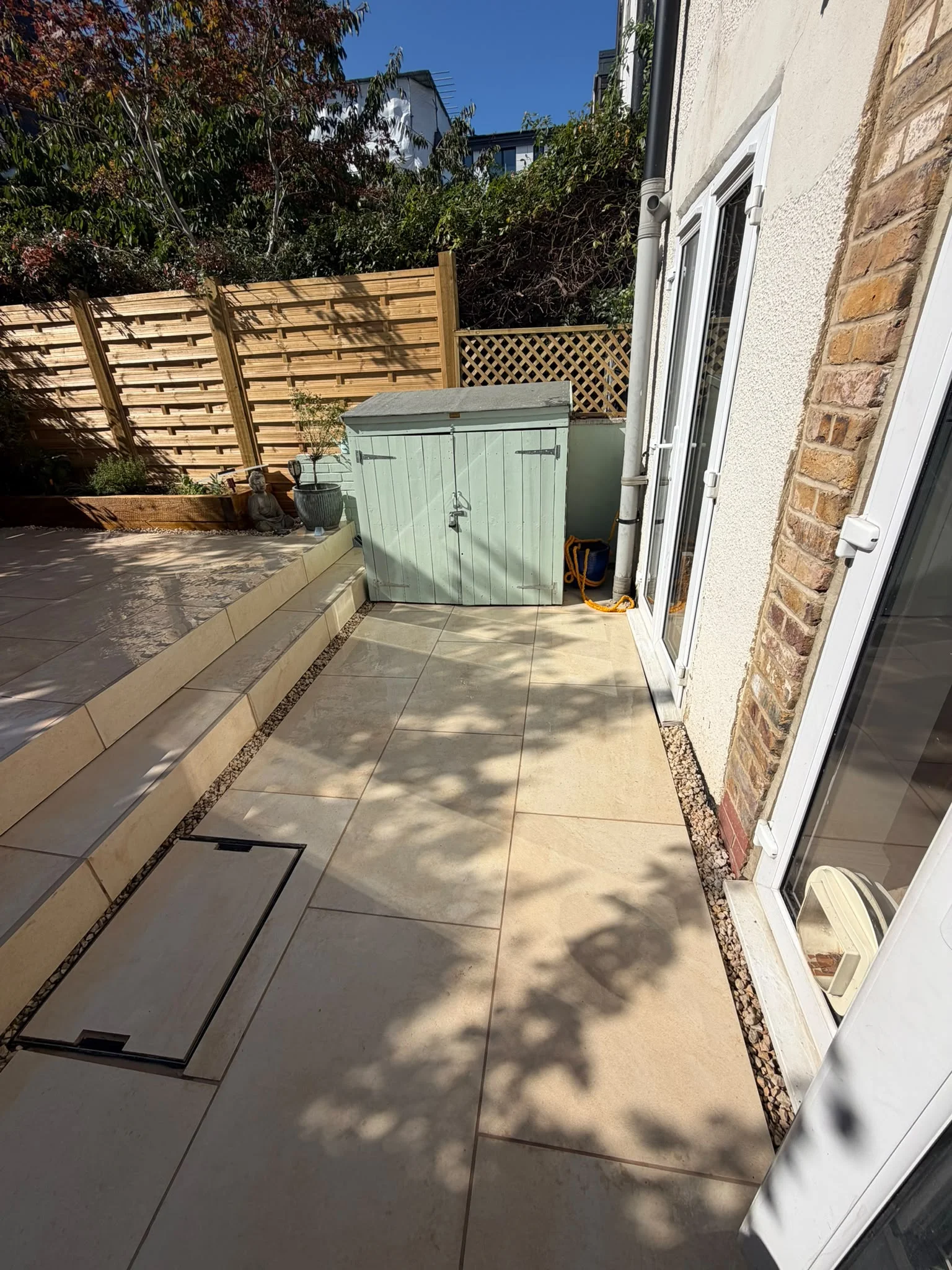 New porcelain patio with French drain gravel drainage channel, trellis fence panel and sage green garden shed in Greenwich