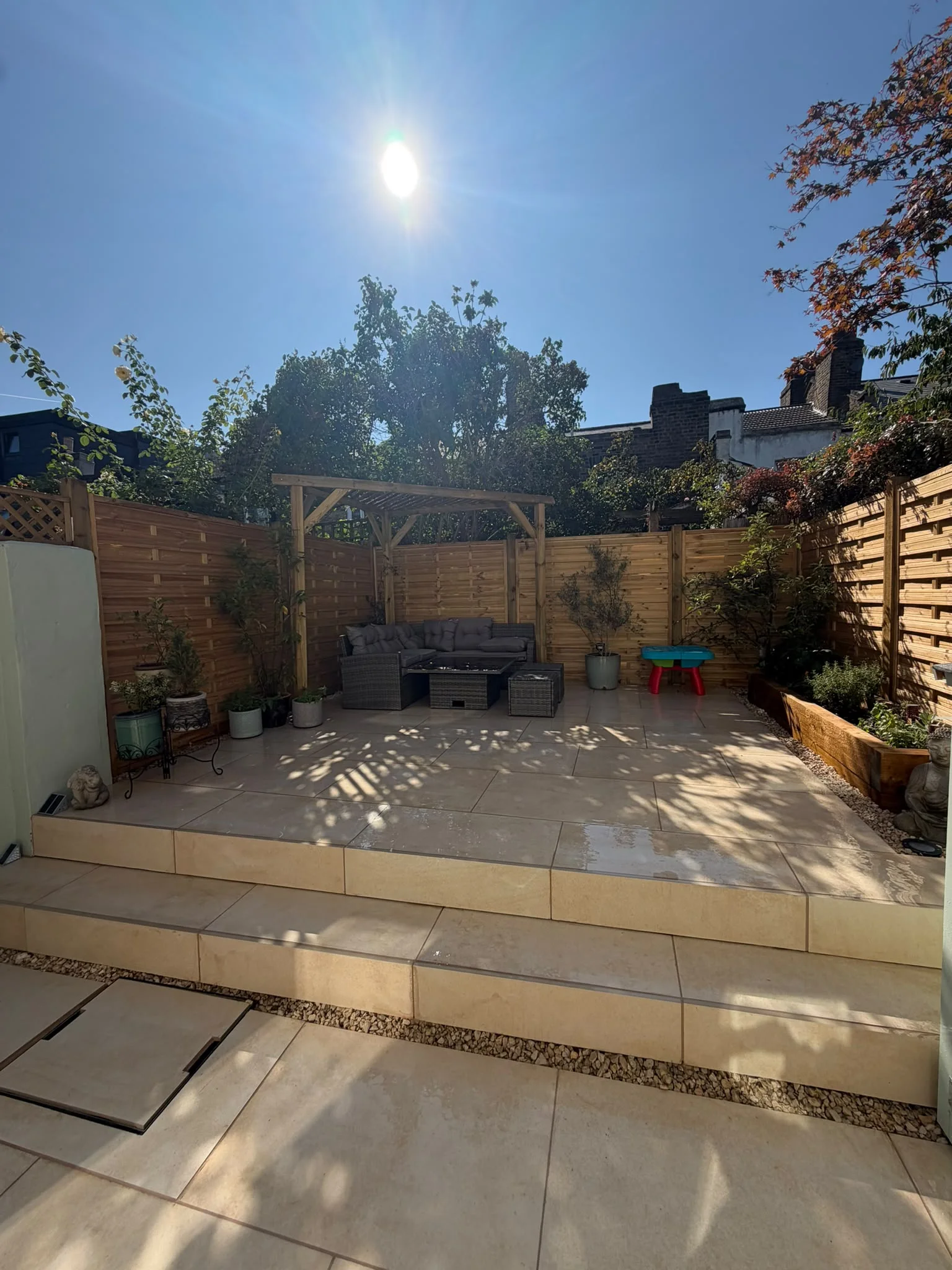 Custom-built timber pergola over a rattan corner sofa on a new porcelain patio in a Greenwich garden landscaping project