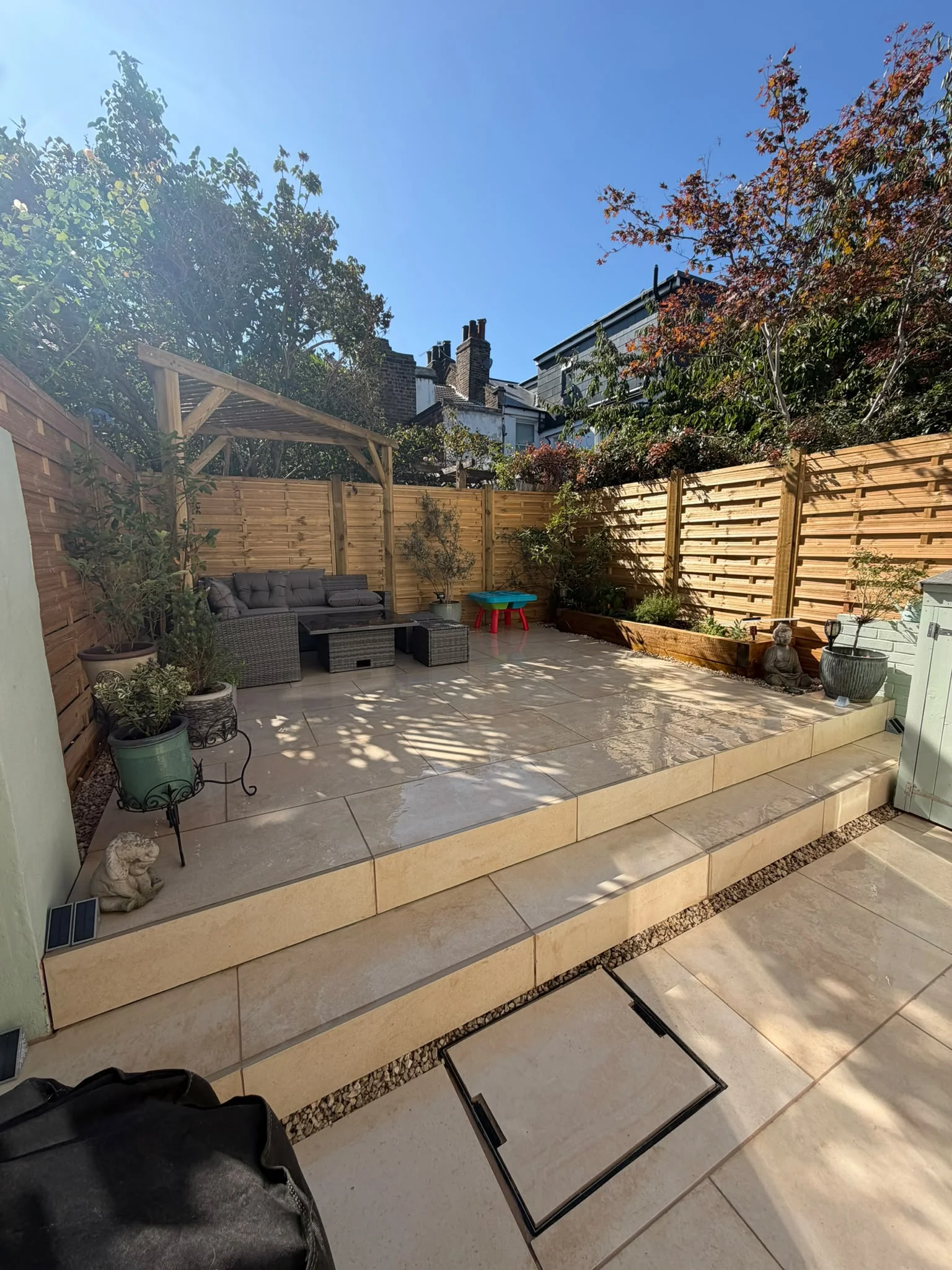 Multi-level new porcelain patio with steps, raised sleeper beds and pergola seating area in a Greenwich garden