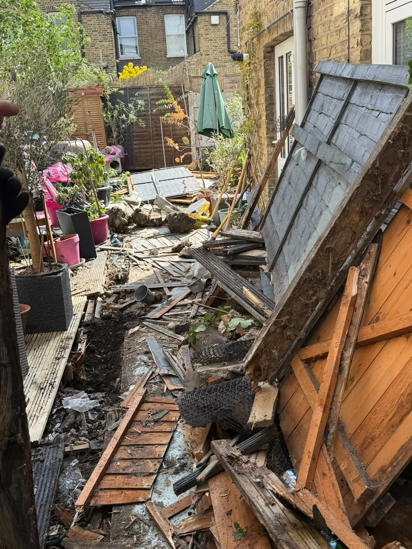 Collapsed garden fence with broken timber panels and failed posts in a South East London garden, before repair